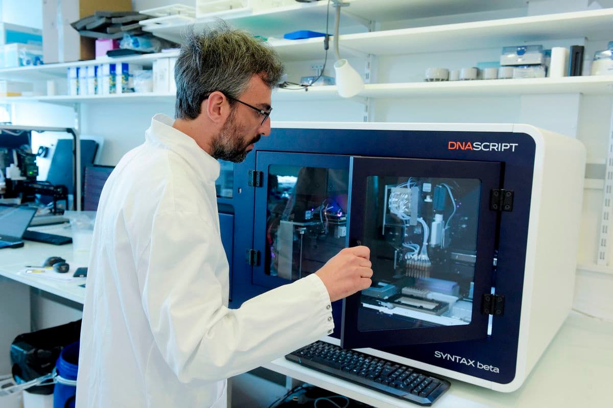 실험복을 입은 한 남성이 실험 장비를 다루고 있다. 그는 배경에 실험 용품과 과학 장비가 가득한 선반이 있는 실험실에 있다.